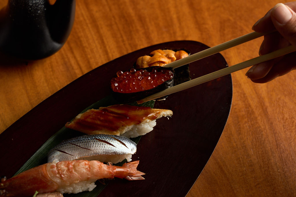 Chopsticks lifting an ikura nigiri from the Anaba omakase tray
